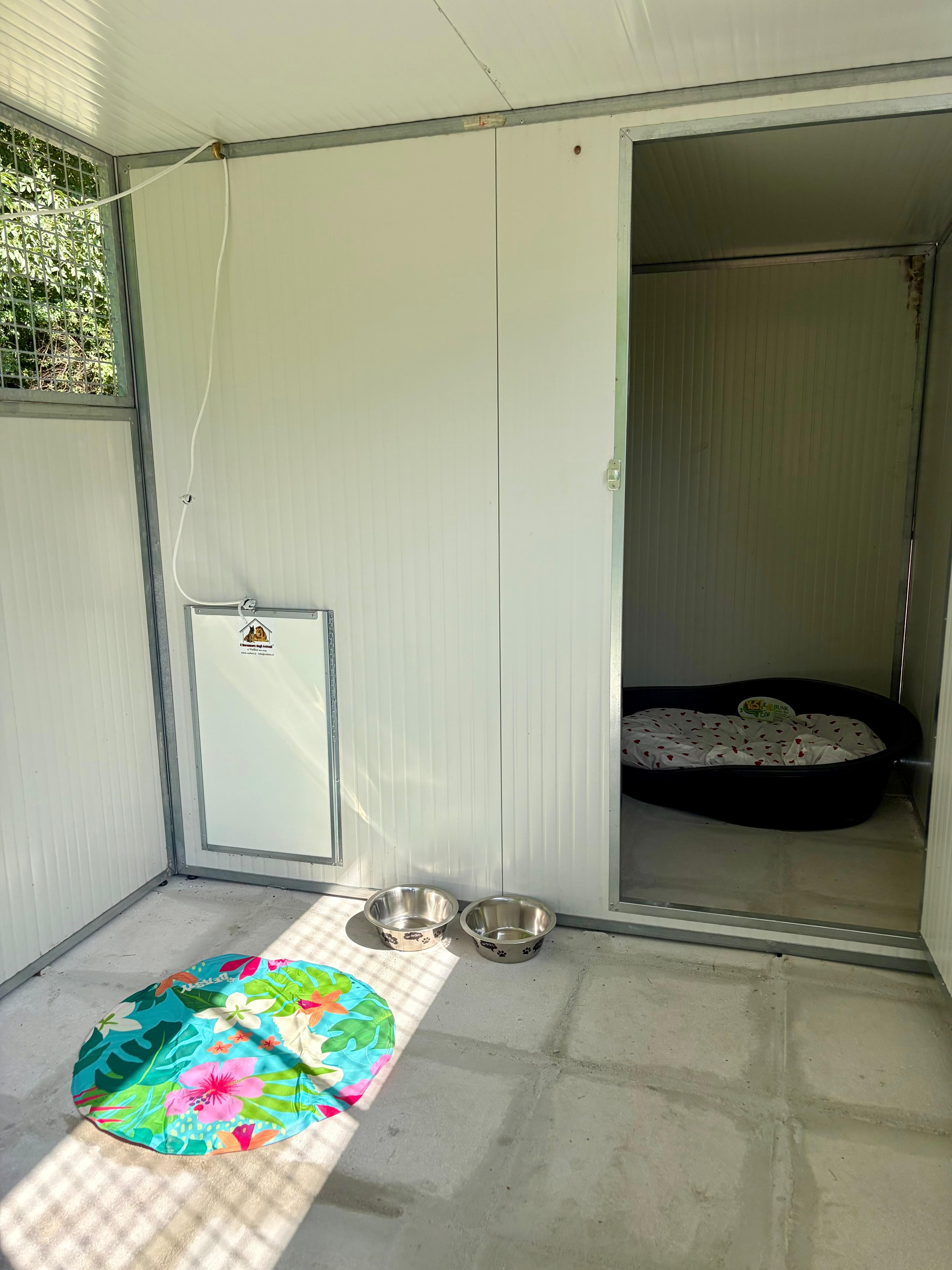 Interno di un box con cuccia, ciotole e area coperta